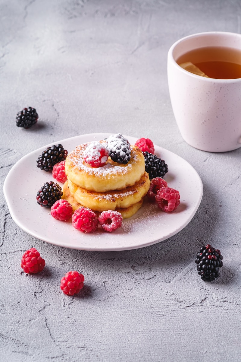 a plate of pancakes with berries and a cup of tea